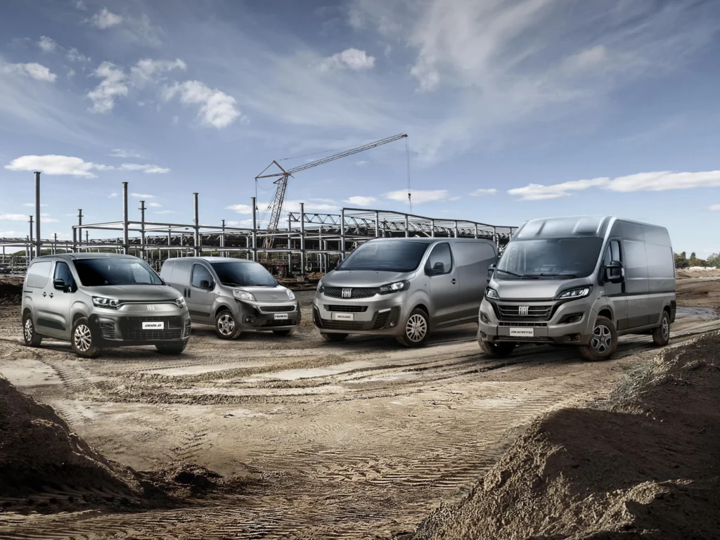 Die verschiedenen Fiat Nutzfahrzeuge Modelle nebeneinander aufgestellt vor einer Baustelle.