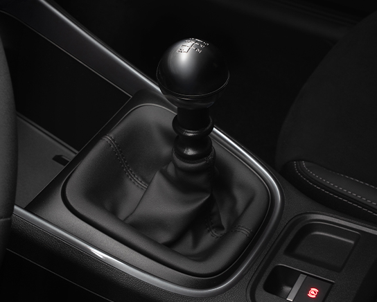 Auf diesem Bild ist der Innenraum eines Autos mit einem manuellen 6-Gang-Schalthebel, Teilen der Mittelkonsole, einem Sitz und dem Knopf für die elektronische Parkbremse zu sehen.